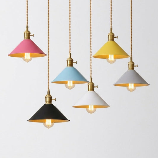 Five hanging pendant lights with cone-shaped shades in pink, yellow, light blue, black, and white, each with a brass fixture and visible bulb, shown against a plain light background.