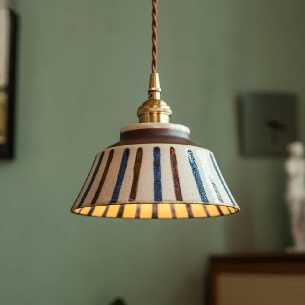Striped pendant light with a gold fixture against a green wall