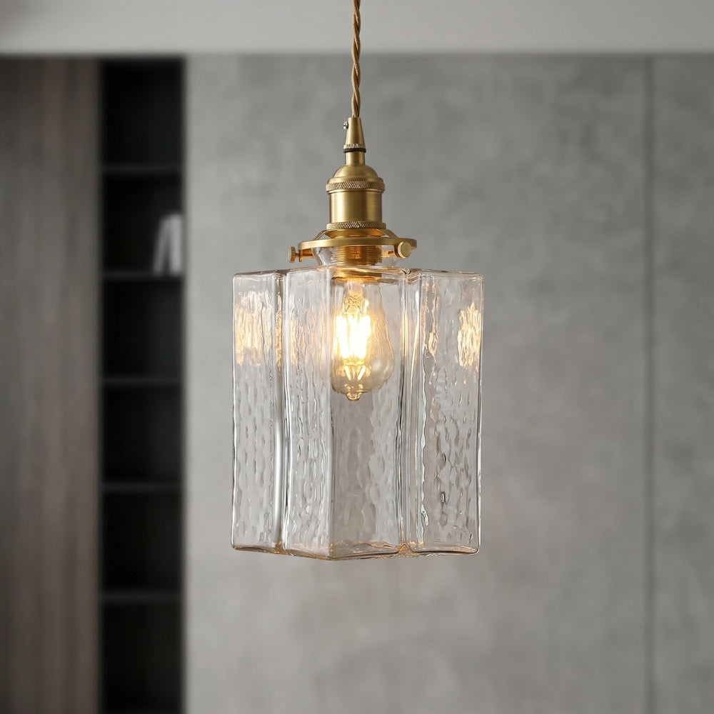 Pendant light with clear glass shade and brass fixture on a neutral background