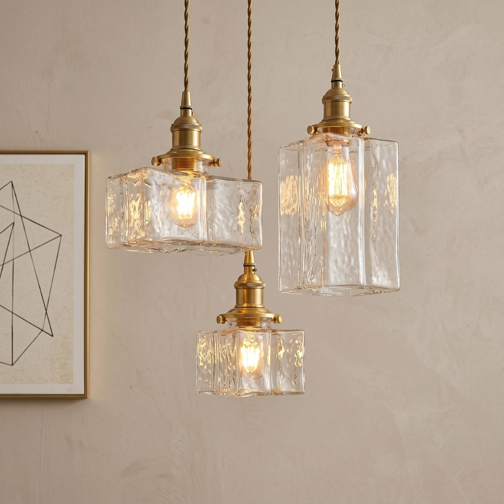 Three pendant lights with glass shades and gold fixtures on a beige wall.