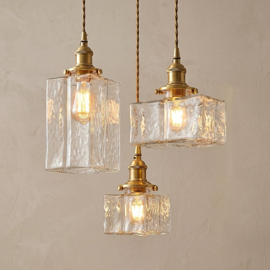 Three pendant lights with clear glass shades and gold fixtures on a beige background