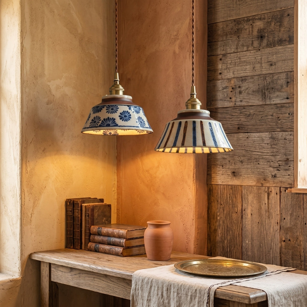 Two pendant lights with decorative shades hanging above a wooden table with books and a vase.