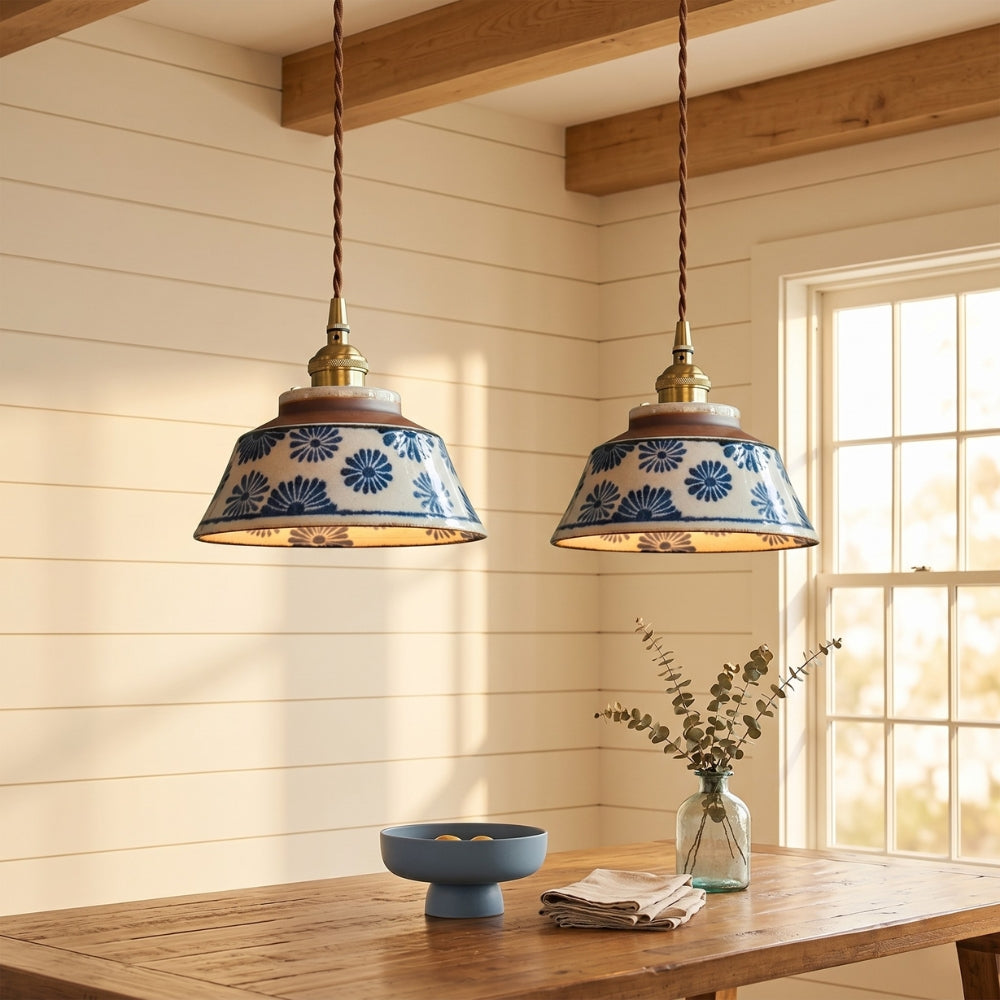 Two pendant lights with floral patterns hanging above a wooden table in a room with wooden beams and a window.