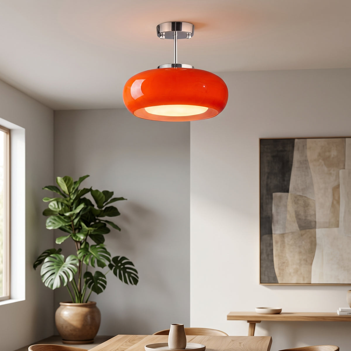A modern orange glass pendant light with a chrome ceiling mount hanging in a minimalist dining room setting.