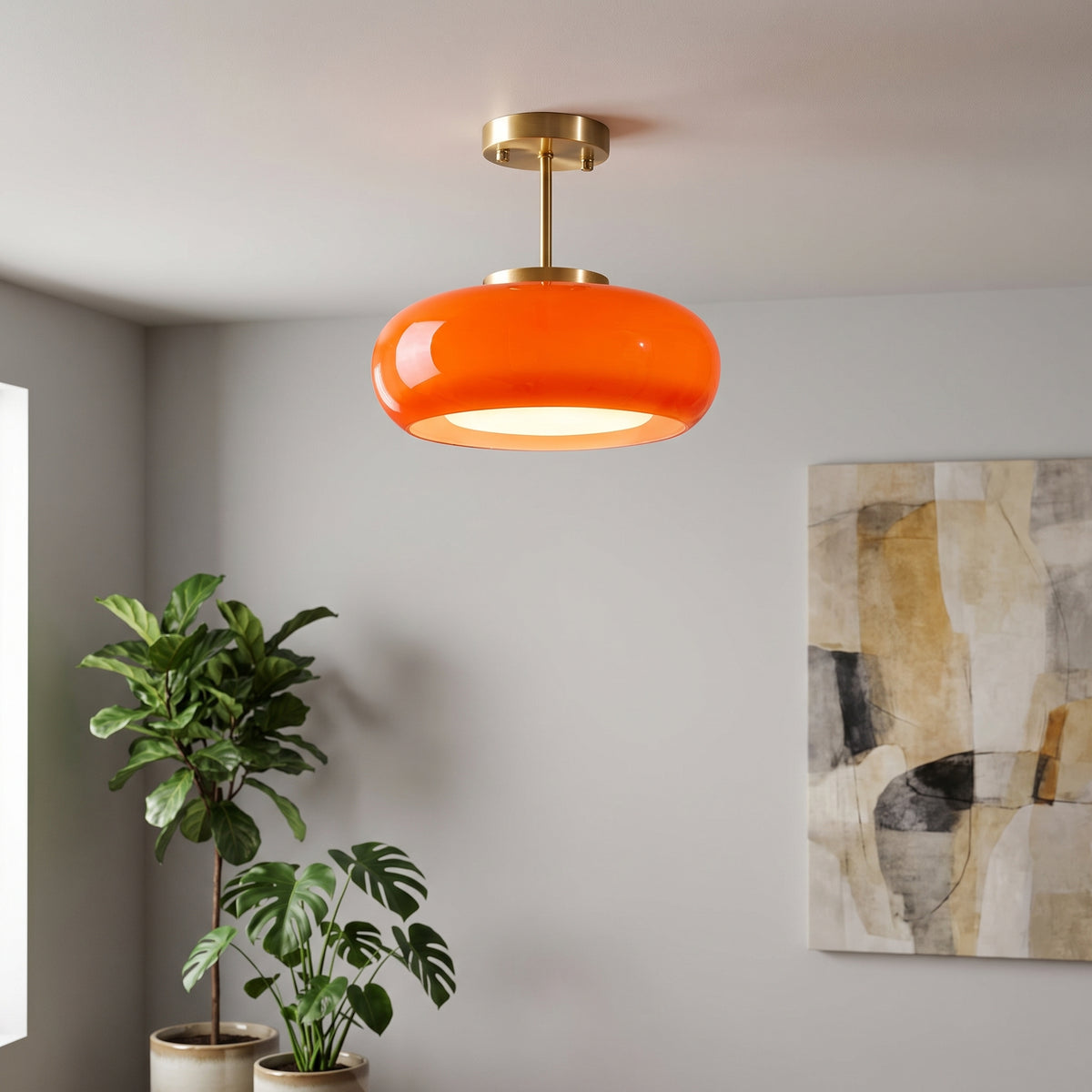 An orange glass pendant light with a brass ceiling mount, shown hanging in a modern room with potted plants and abstract wall art.