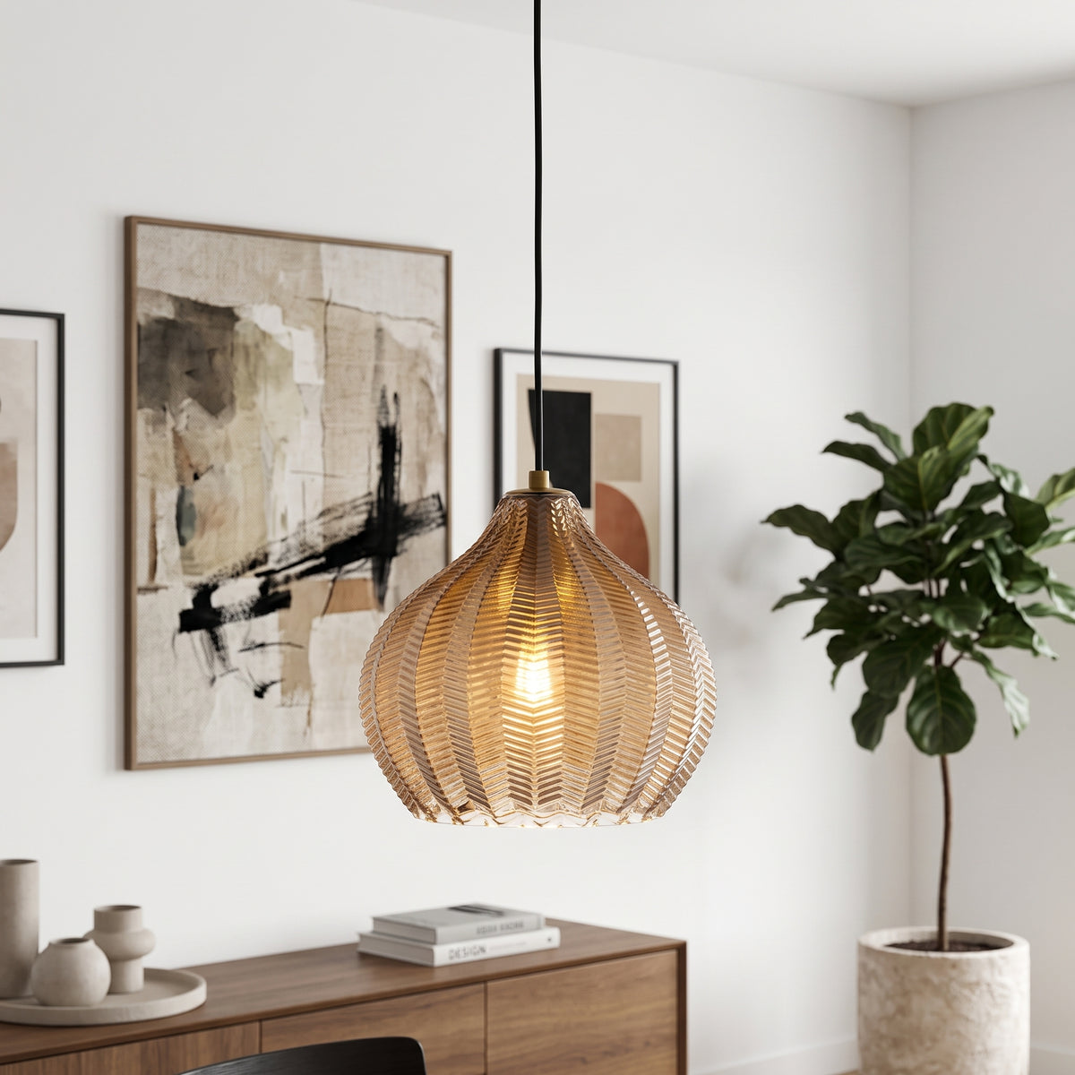 A hanging pendant light with a ribbed, woven metallic gold shade suspended by a black cord in a modern, sunlit room with framed abstract art and a potted plant.
