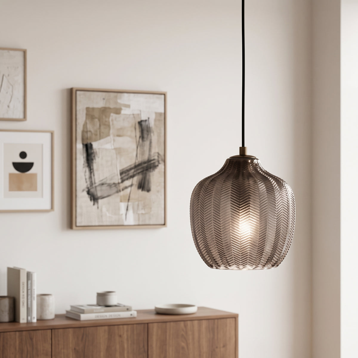 A modern pendant light with a textured, ribbed metallic shade hanging in a minimalist room with a wooden console table and framed abstract wall art.