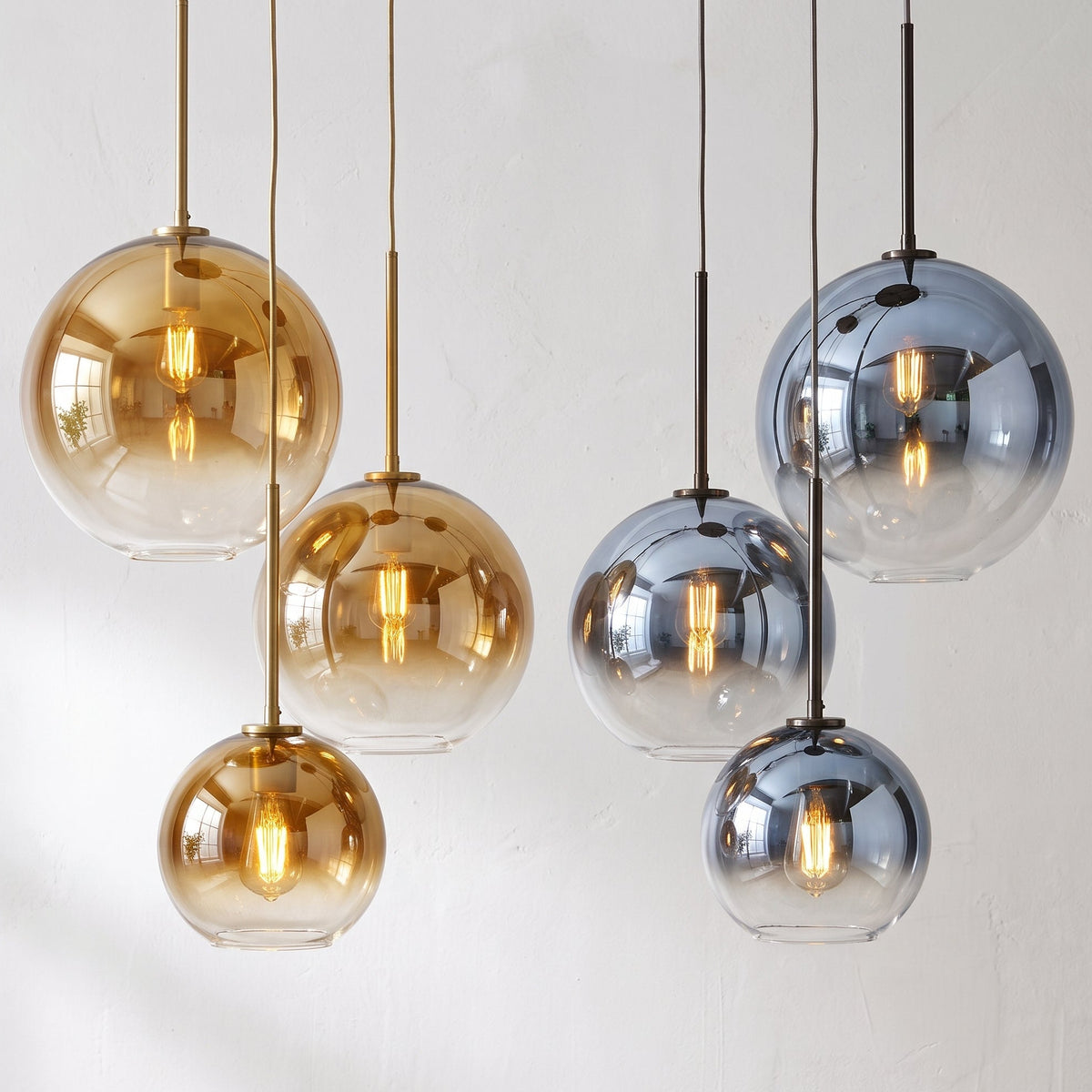 Five spherical pendant light bulbs in smoked glass, three in warm amber-tinted glass and two in cool smoky blue-gray glass, hanging from black cords against a light wall.