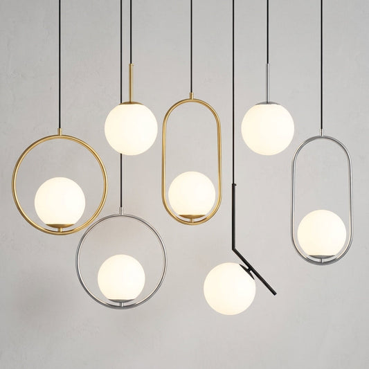 A set of modern pendant lights with spherical frosted white glass globes suspended in various geometric metal frames, including gold and silver, against a neutral light gray wall.