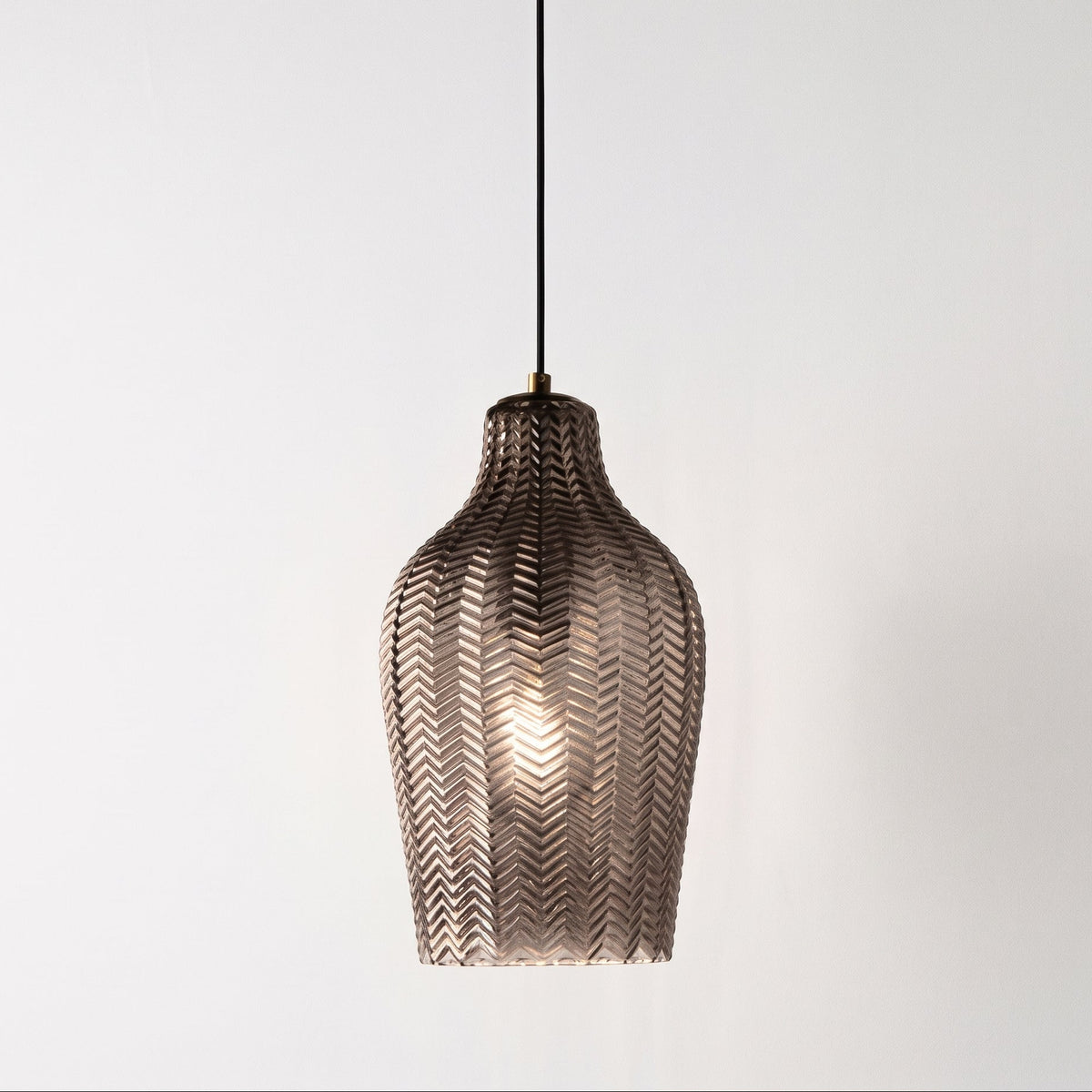 A hanging pendant light with a textured, woven metallic shade in a bronze finish, suspended by a black cord against a plain white background.