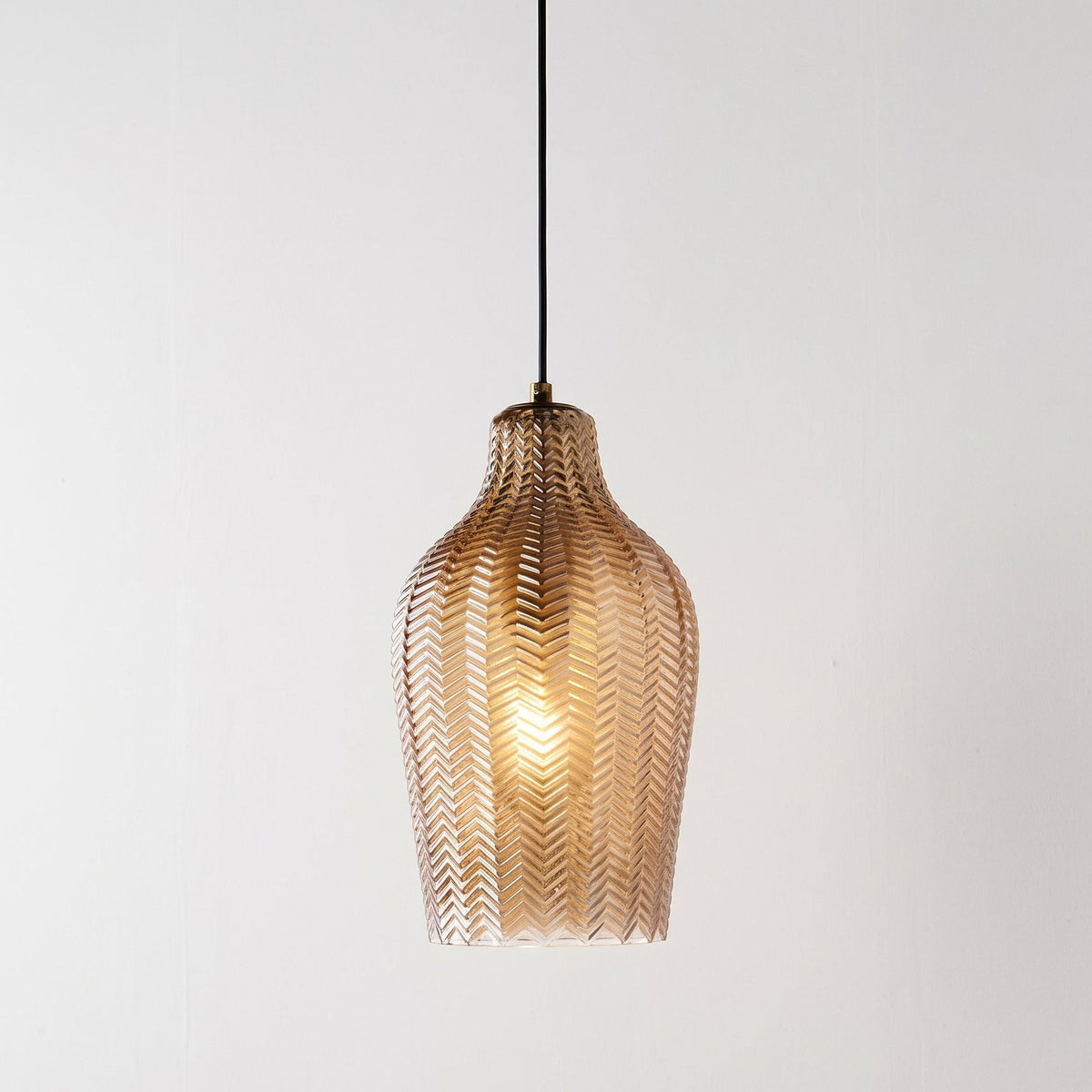 A modern pendant light with a textured, woven metallic shade in a warm bronze finish, suspended by a thin black cord against a plain white background.
