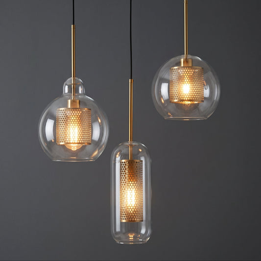 Three modern pendant lights with clear glass globes and cylindrical shades, featuring gold-toned metal rods and illuminated perforated inner cylinders, shown against a dark gray background.