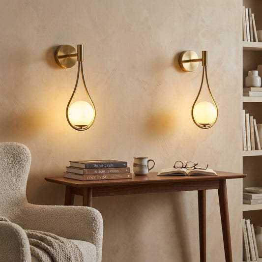 Two gold wall sconces on a beige wall with a wooden table and books in the foreground.