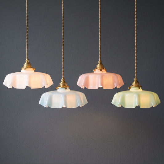 Four hanging pendant lights with fluted glass shades in white, pale pink, pale blue, and pale yellow, suspended by gold-toned cords against a dark gray wall.
