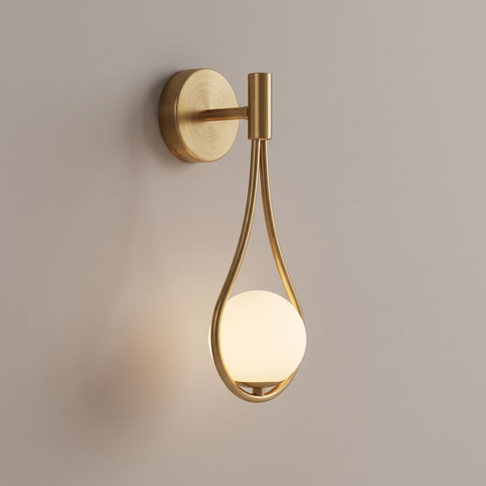 A modern wall sconce with a brushed gold metal frame and a glowing frosted glass globe, mounted on a plain warm beige wall.